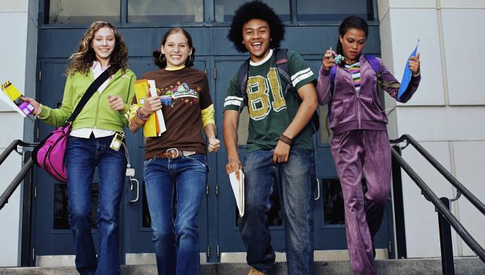 4 young teens leaving school with books and backpacks, all smiling