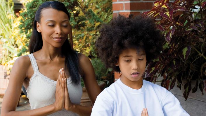 A mother and son sit with their eyes closed and their palms pressed together