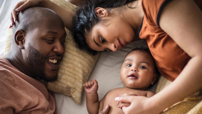 Parents lay with their infant on a bed.