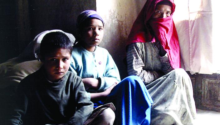 An Afghan woman in a headscarf huddles with her two grandchildren on the floor