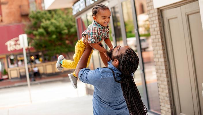 On a Baltimore street, a father lifts his young son up in the air. Both are smiling.