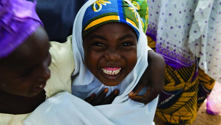 A mother in a purple headscarf and her smiling daughter in a white scarf