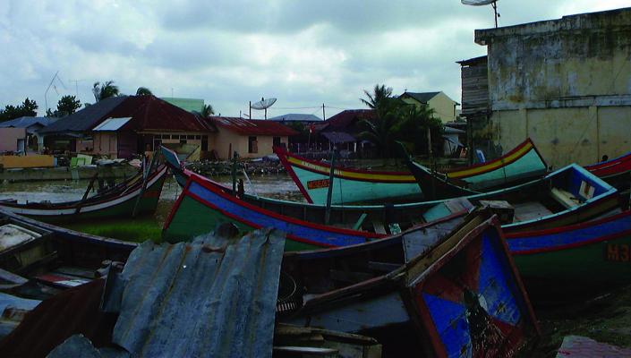 boats and debris such as corrugated metal are tossed on land next to a brick concrete building