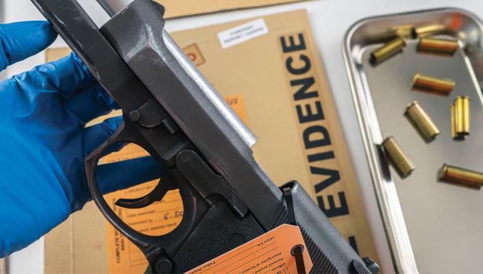 a gloved hand holds a handgun next to a tray of bullets