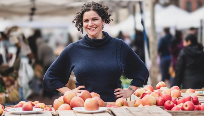 Julia Wolfson standing in front of fruit at an outdoor market.