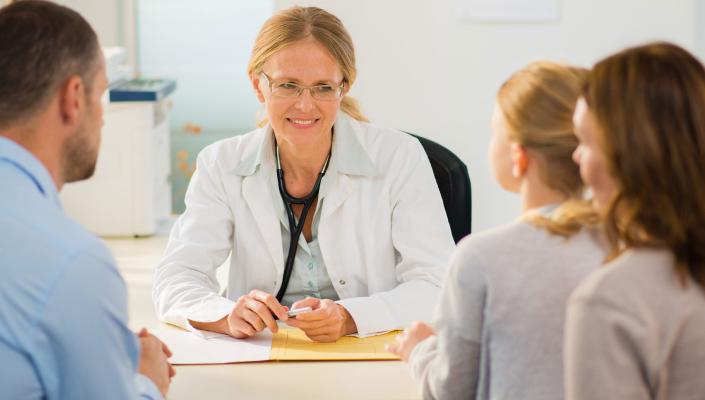 a female pediatrician talks with parents and their young daughter