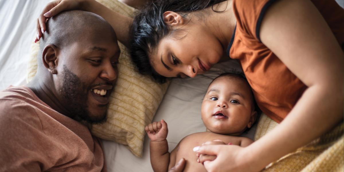 Parents lay with their infant on a bed.