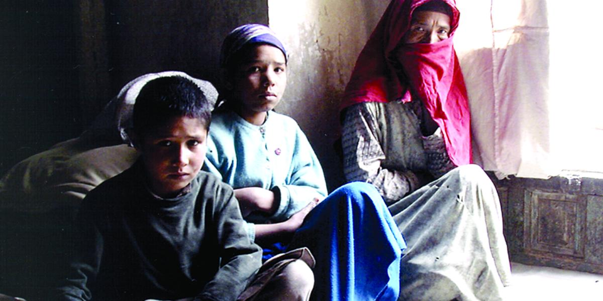 An Afghan woman in a headscarf huddles with her two grandchildren on the floor