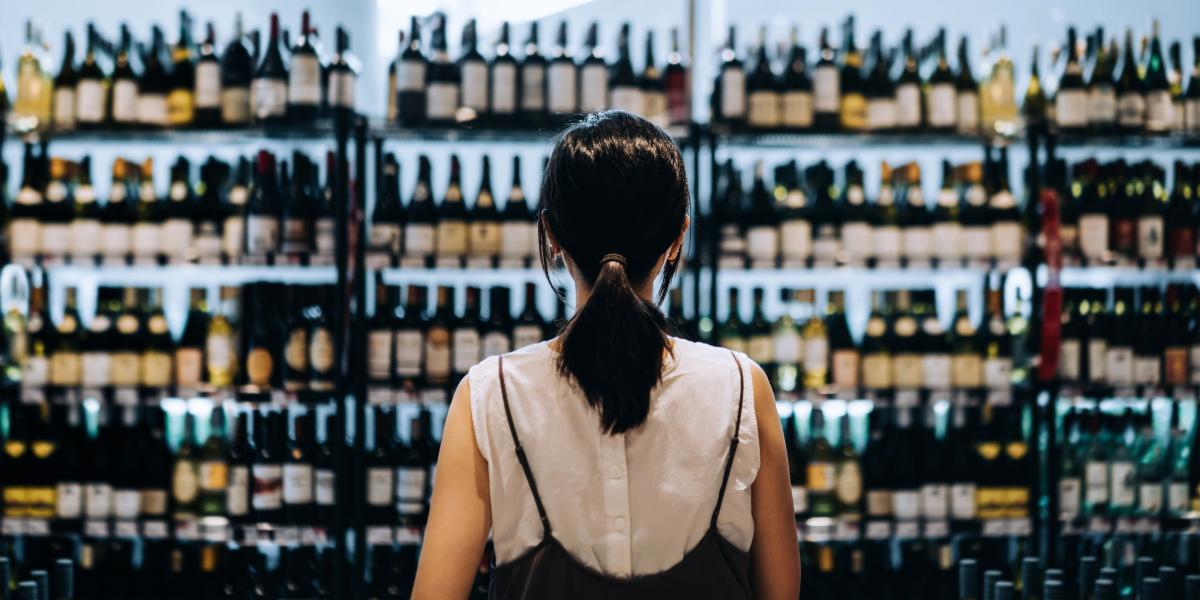 A review of a young woman who is standing in front of a shelf full of alcohol in a grocery store.