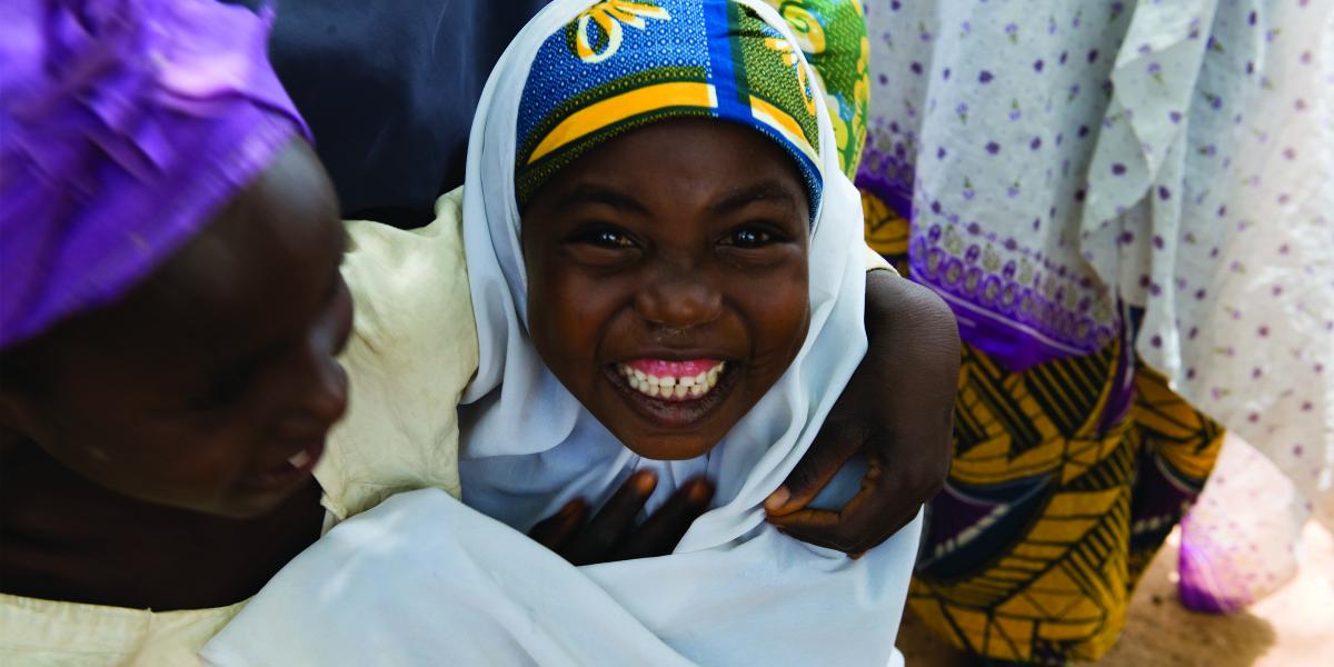 A mother in a purple headscarf and her smiling daughter in a white scarf