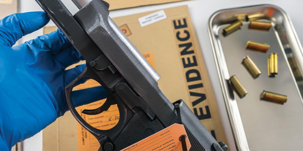 a gloved hand holds a handgun next to a tray of bullets