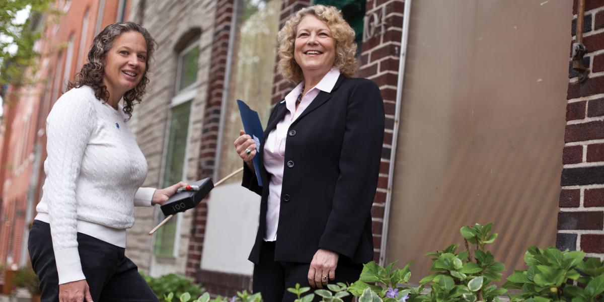 Wendy Shields and Andrea Gielen stand at the entrance to a rowhome in Baltimore