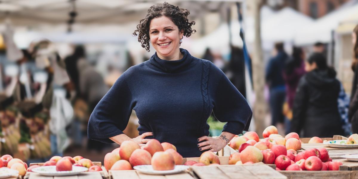 Julia Wolfson standing in front of fruit at an outdoor market.