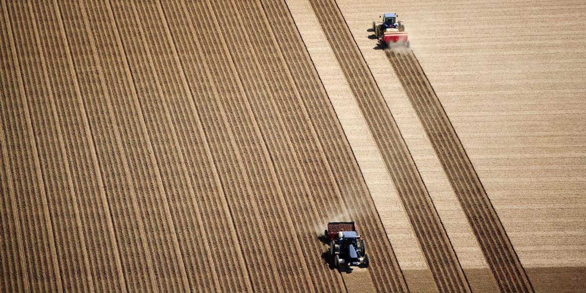 Aerial view of 2 tractors planting potatoes in the fertile farm fields of Idaho, during the spring.