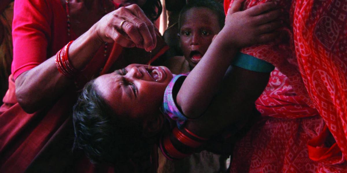 a crying Nepalese child is held with his head back to receive vitamin A drops in his mouth