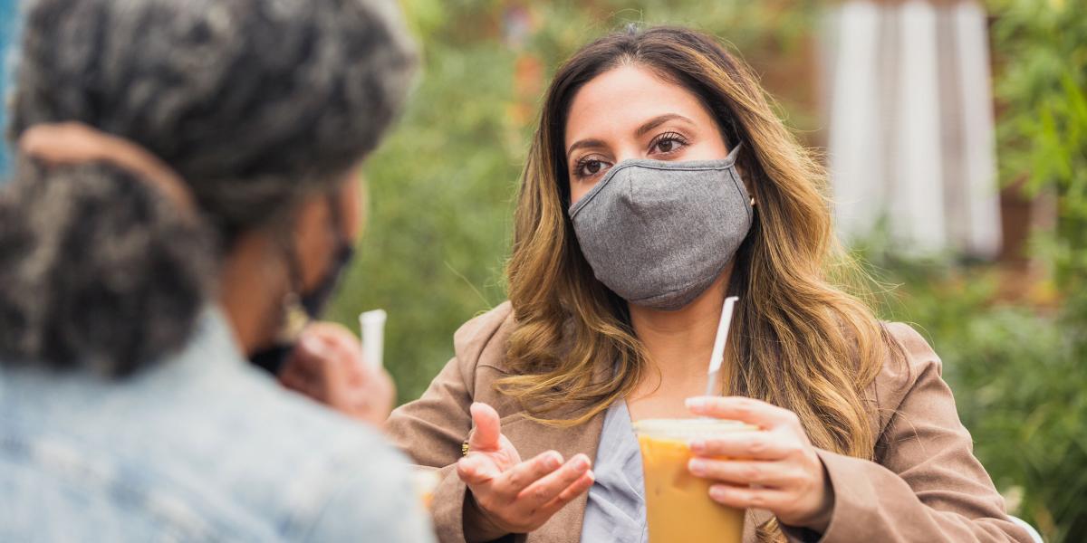 A woman wearing a mask speaks and gestures to a friend