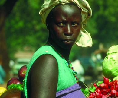 An African woman in a produce market carries her baby in a wrap on her back