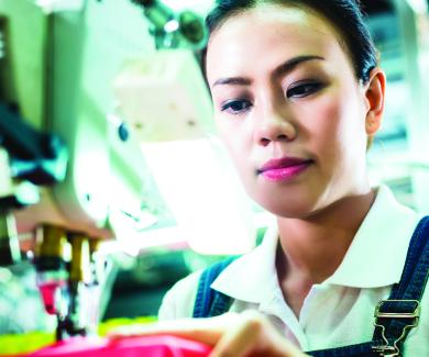 a female textile worker at a sewing machine stitches a red garment