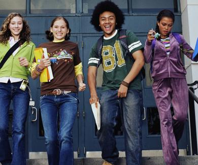 4 young teens leaving school with books and backpacks, all smiling