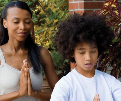 A mother and son sit with their eyes closed and their palms pressed together