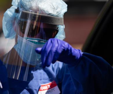 person with plastic face shield, gloves, and covid test swab