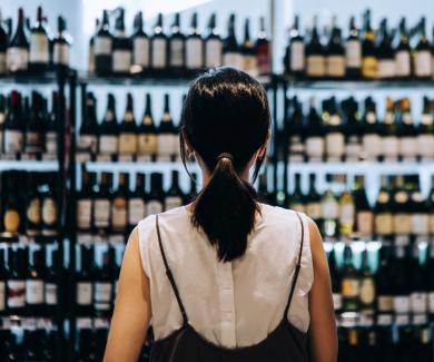 A review of a young woman who is standing in front of a shelf full of alcohol in a grocery store.