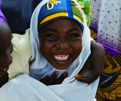 A mother in a purple headscarf and her smiling daughter in a white scarf