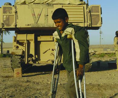 A young teen on crutches walks by a military vehicle guarded by a soldier