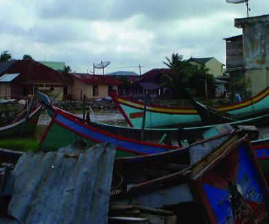 boats and debris such as corrugated metal are tossed on land next to a brick concrete building