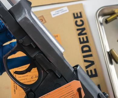 a gloved hand holds a handgun next to a tray of bullets