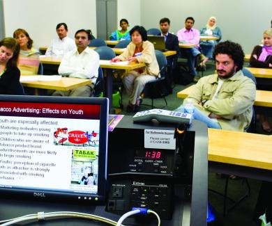 Students in a classroom listen to a talk on Tobacco Advertising: Effects on Youth, which is visible on the presenter's laptop monitor