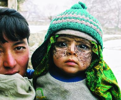 A mother holding her son, who wears a knit cap and a paste on his face as protection from the cold