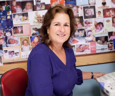 Janet DiPietro with a corkboard filled with baby pictures behind her