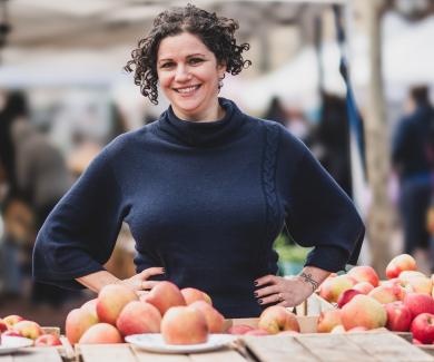 Julia Wolfson standing in front of fruit at an outdoor market.