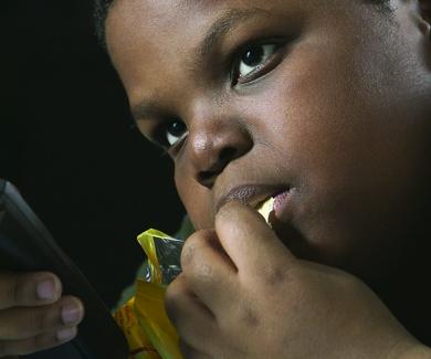 A young boy snacks on chips with a TV remote in his hand