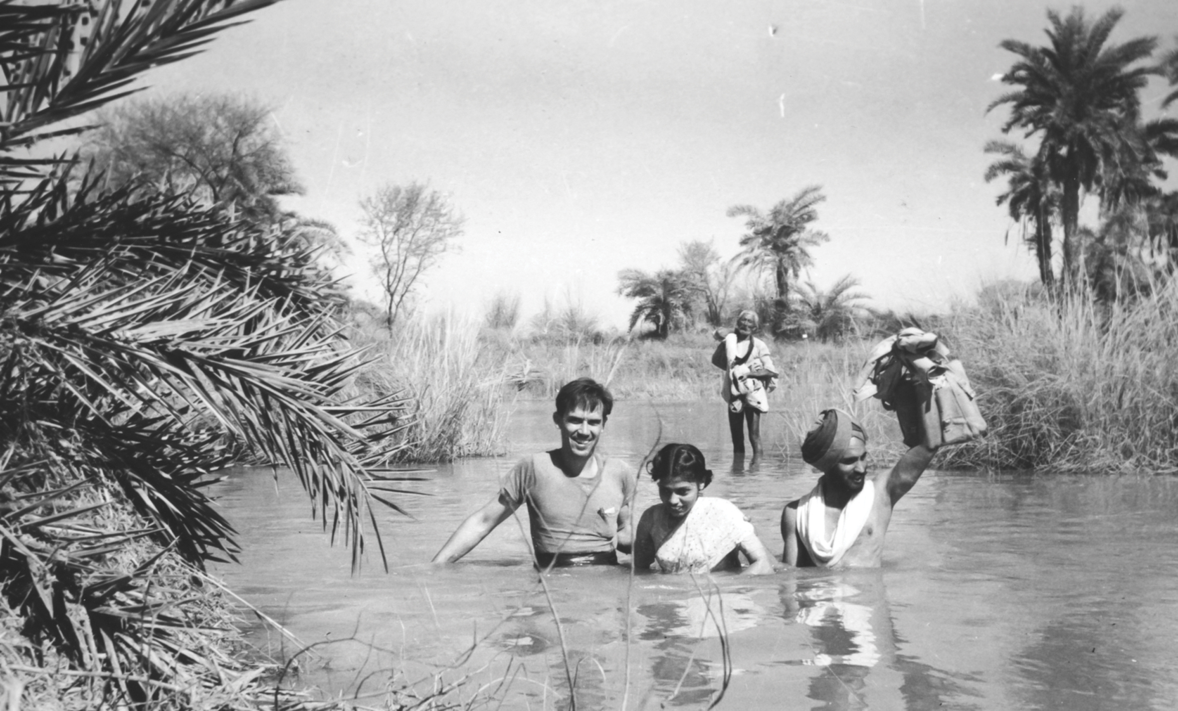 A black and white photograph of Carl Taylor, founding chair of the Department of International Health standing in a lake with two other people.